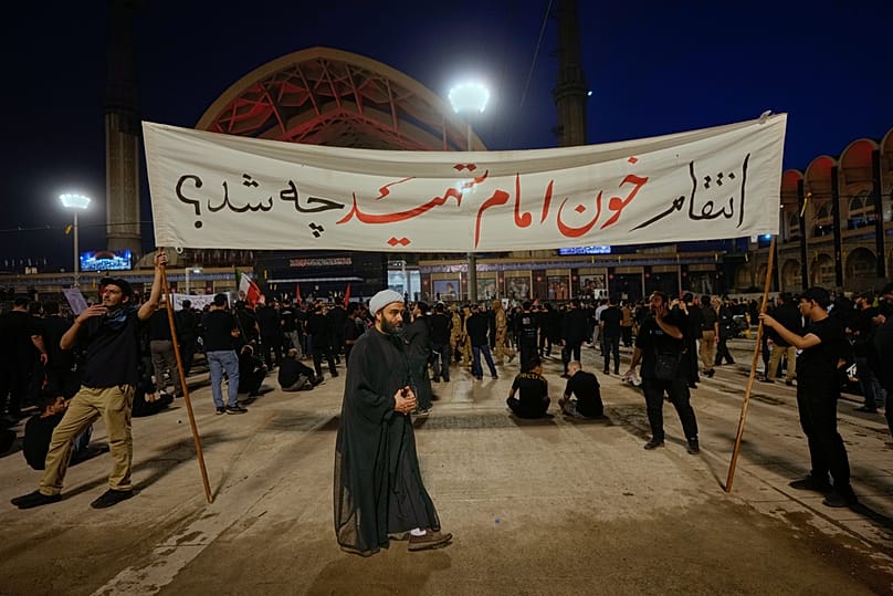 يمر رجل دين أمام مشيعين يحملون لافتة كُتب عليها "ما هو القصاص لاستشهاد إمامنا؟" وذلك خلال مراسم تشييع المرشد الأعلى الإيراني الراحل علي خامنئي إيران، يوم السبت 4 يوليو 2026.