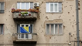 A Bosnian flag waves on a Sarajevo building scarred by bullet and shelling damage from the 1992-1995 war.