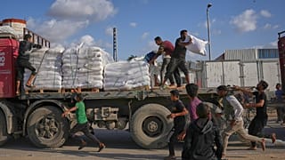 فلسطينيون يحصلون على أكياس طحين من شاحنة مساعدات تابعة لبرنامج الأغذية العالمي أثناء مرورها في دير البلح وسط قطاع غزة، في 15 نوفمبر 2025.