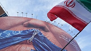 A man waves an Iranian flag under a billboard with graphic showing Strait of Hormuz and sewn lips of US President Donald Trump in Tehran, Iran, Wednesday, May 6, 2026. 