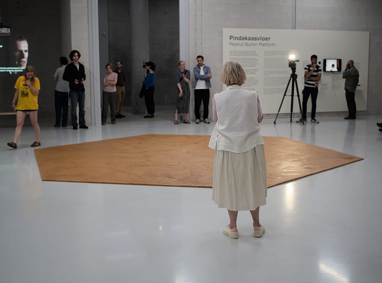 Pessoas observam o chão de manteiga de amendoim espalhado pelo piso do museu em homenagem ao artista neerlandês Wim T. Schippers