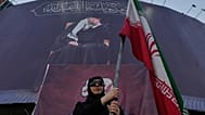امرأة موالية للحكومة تحمل العلم الإيراني تحت لافتة تظهر صورة المرشد الأعلى الراحل آية الله علي خامنئي