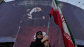 امرأة موالية للحكومة تحمل العلم الإيراني تحت لافتة تظهر صورة المرشد الأعلى الراحل آية الله علي خامنئي