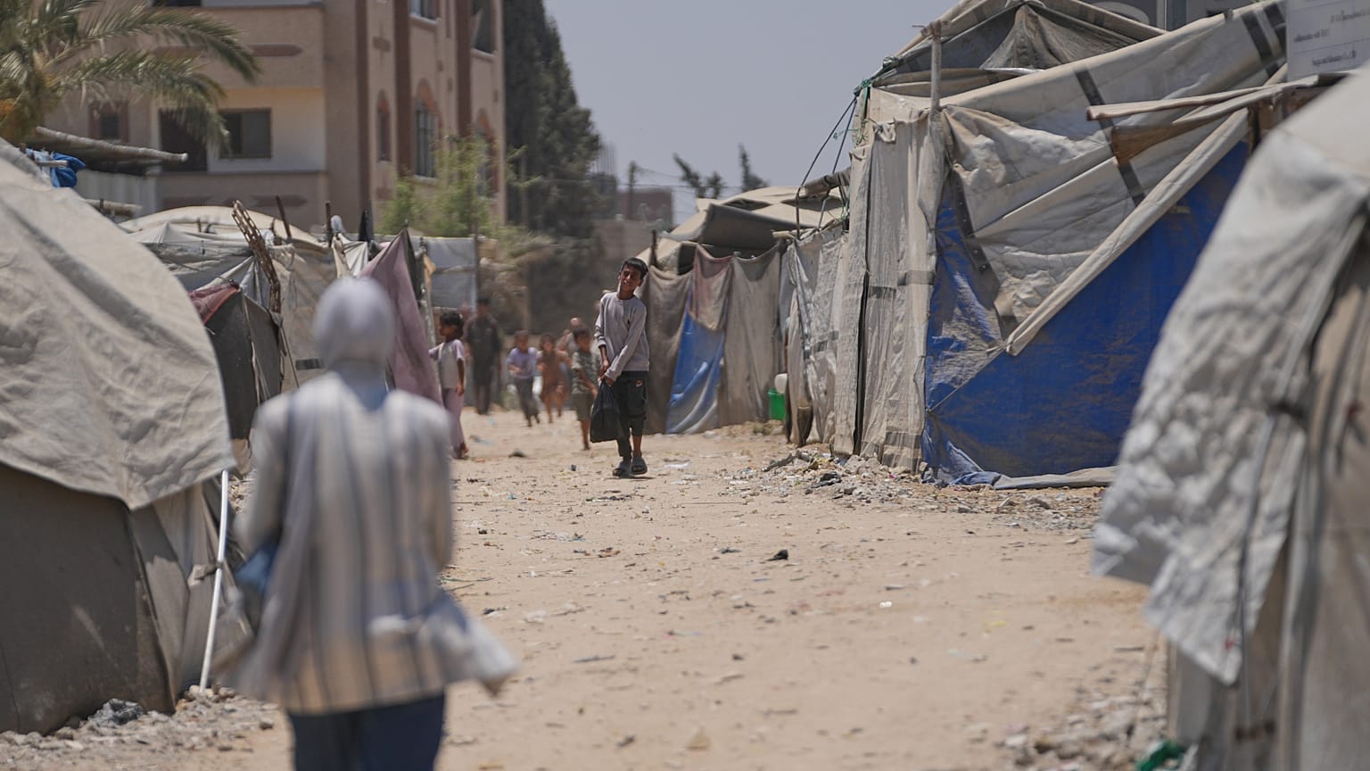 نازحون فلسطينيون يسيرون بين الخيام في دير البلح بوسط قطاع غزة، السبت 4 يوليو 2026. (AP Photo/عبد الكريم حنا)