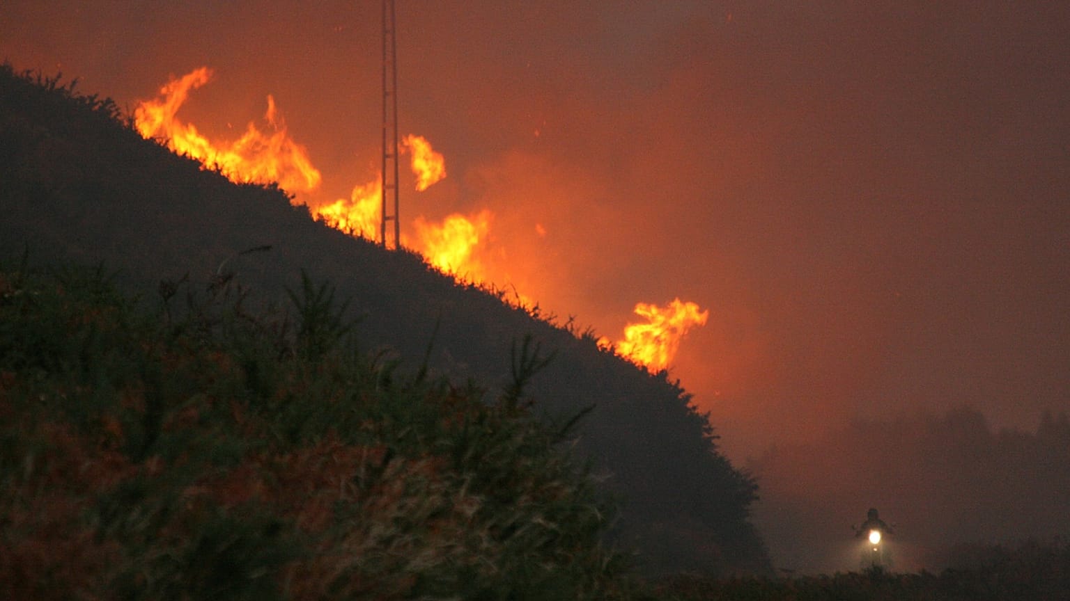Un motorista cruza la carretera que baja de la cima, ya cubierta por el humo del incendio forestal en el Monte do Faro, en Valença do Minho (Portugal) 
