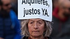 Egy nő a fején egy spanyol nyelvű táblát visel, amelyen ez olvasható: „Méltányos bérleti díjakat most”, a 2025-ös lakbéremelés elleni tüntetésen.