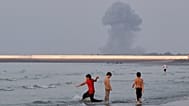 Three boys play in the shallow waters of the Strait of Hormuz, as a plume of smoke rises from an explosion in the background, off Bandar Abbas, Iran, Monday, July 13, 2026. 