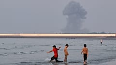 Tres chicos juegan en aguas poco profundas del estrecho de Ormuz mientras una columna de humo se eleva tras una explosión frente a Bandar Abbas, Irán, 13 de julio de 2026.