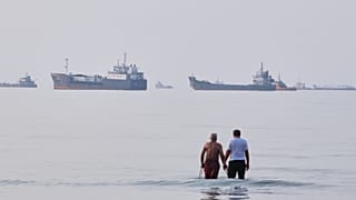 Two men wade in the waters of the Strait of Hormuz with vessels anchored in the background, off Bandar Abbas, Iran, Sunday, July 12, 2026.
