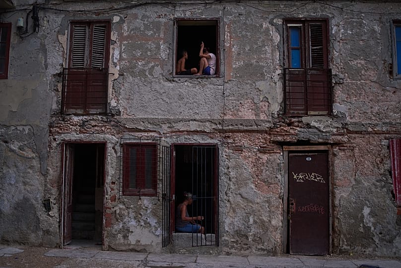 People catch the cool air from the street at their home's window during a blackout in Havana, 10 July, 2026