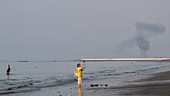 Una mujer permanece en la orilla del estrecho de Ormuz mientras una columna de humo se eleva tras una explosión cerca de Bandar Abbas, Irán, 13 de julio de 2026