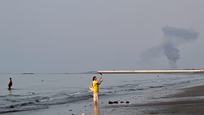 Badende am Ufer der Straße von Hormus, im Hintergrund Rauch nach einer Explosion vor Bandar Abbas im Iran, Montag, 13. Juli 2026