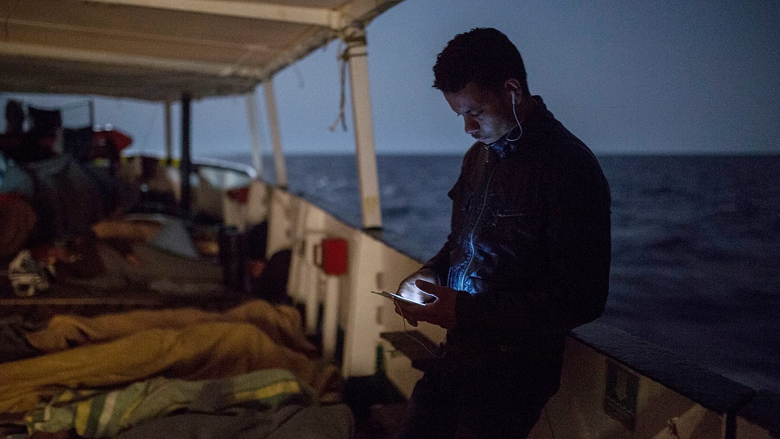 ARCHIVO: Un inmigrante revisa su móvil mientras otros duermen en la cubierta de un barco de la ONG Proactiva Open Arms, el 1 de julio de 2018.