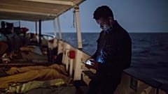 ARCHIVO: Un inmigrante revisa su móvil mientras otros duermen en la cubierta de un barco de la ONG Proactiva Open Arms, el 1 de julio de 2018.