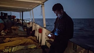ARCHIVO: Un inmigrante revisa su móvil mientras otros duermen en la cubierta de un barco de la ONG Proactiva Open Arms, el 1 de julio de 2018.