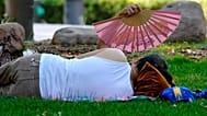FILE: A woman uses a fan to cool off next to a man lying down in a park in Madrid, Spain.