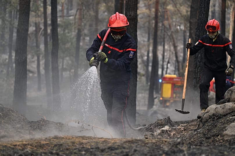 Un pompier arrose les braises après un incendie de forêt dans la région de la forêt de Fontainebleau, au sud de Paris, en France, mardi 14 juillet 2026. 