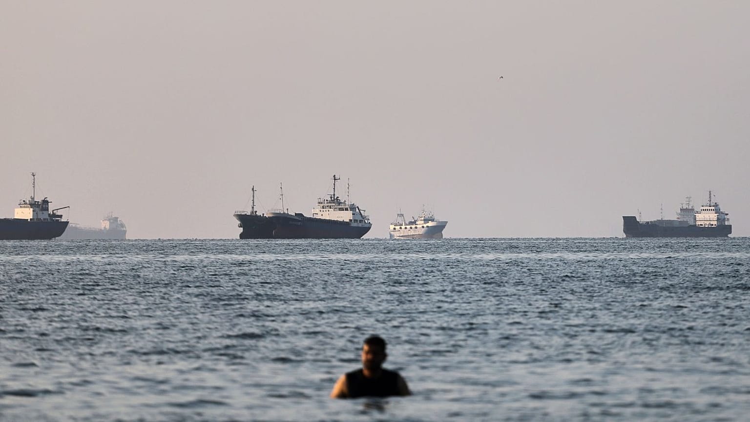 A person stands in shallow water as cargo and commercial vessels are anchored in the Strait of Hormuz off Bandar Abbas, Iran, Monday, June 8, 2026. (Amirhosein Khorgooi/ISNA v