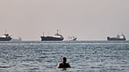A person stands in shallow water as cargo and commercial vessels are anchored in the Strait of Hormuz off Bandar Abbas, Iran, Monday, June 8, 2026. (Amirhosein Khorgooi/ISNA v