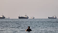 A person stands in shallow water as cargo and commercial vessels are anchored in the Strait of Hormuz off Bandar Abbas, Iran, Monday, June 8, 2026. (Amirhosein Khorgooi/ISNA v