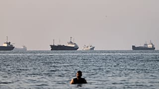 A person stands in shallow water as cargo and commercial vessels are anchored in the Strait of Hormuz off Bandar Abbas, Iran, Monday, June 8, 2026. (Amirhosein Khorgooi/ISNA v
