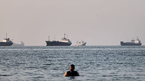 A person stands in shallow water as cargo and commercial vessels are anchored in the Strait of Hormuz off Bandar Abbas, Iran, Monday, June 8, 2026. (Amirhosein Khorgooi/ISNA v