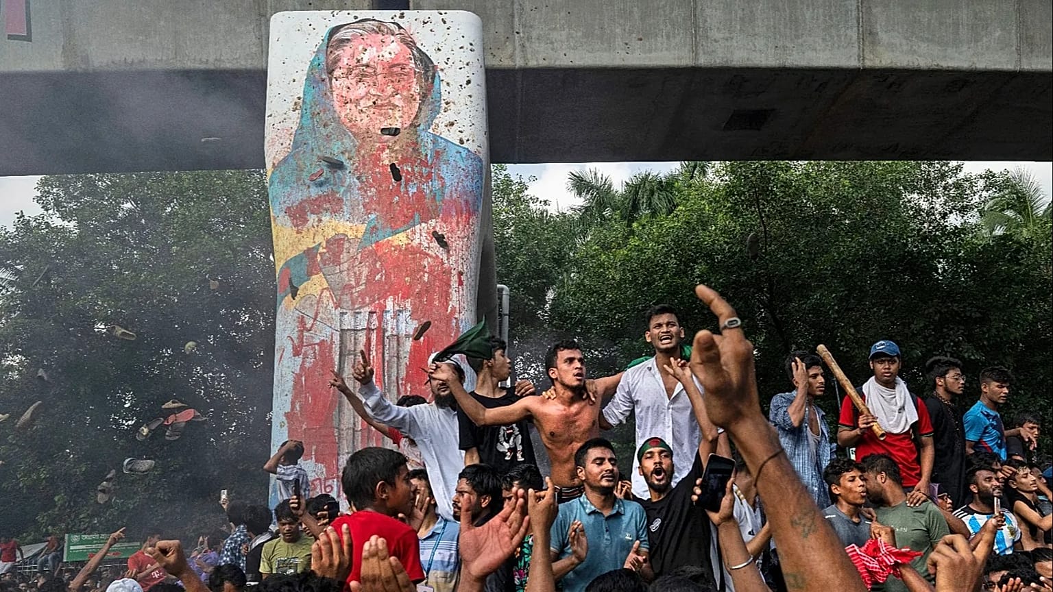  متظاهرون يحتفلون بجانب صورة مشوهة لرئيسة الوزراء الشيخة حسينة بعد أنباء استقالتها، في دكا، بنغلاديش، الاثنين 5 أغسطس 2024.