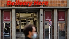 صورة أرشيفية - رجل يرتدي كمامة يقف أمام مدخل مقر شركة توصيل الطعام "Delivery Hero" في برلين بألمانيا، يوم الأربعاء 28 تشرين الأول 2020.