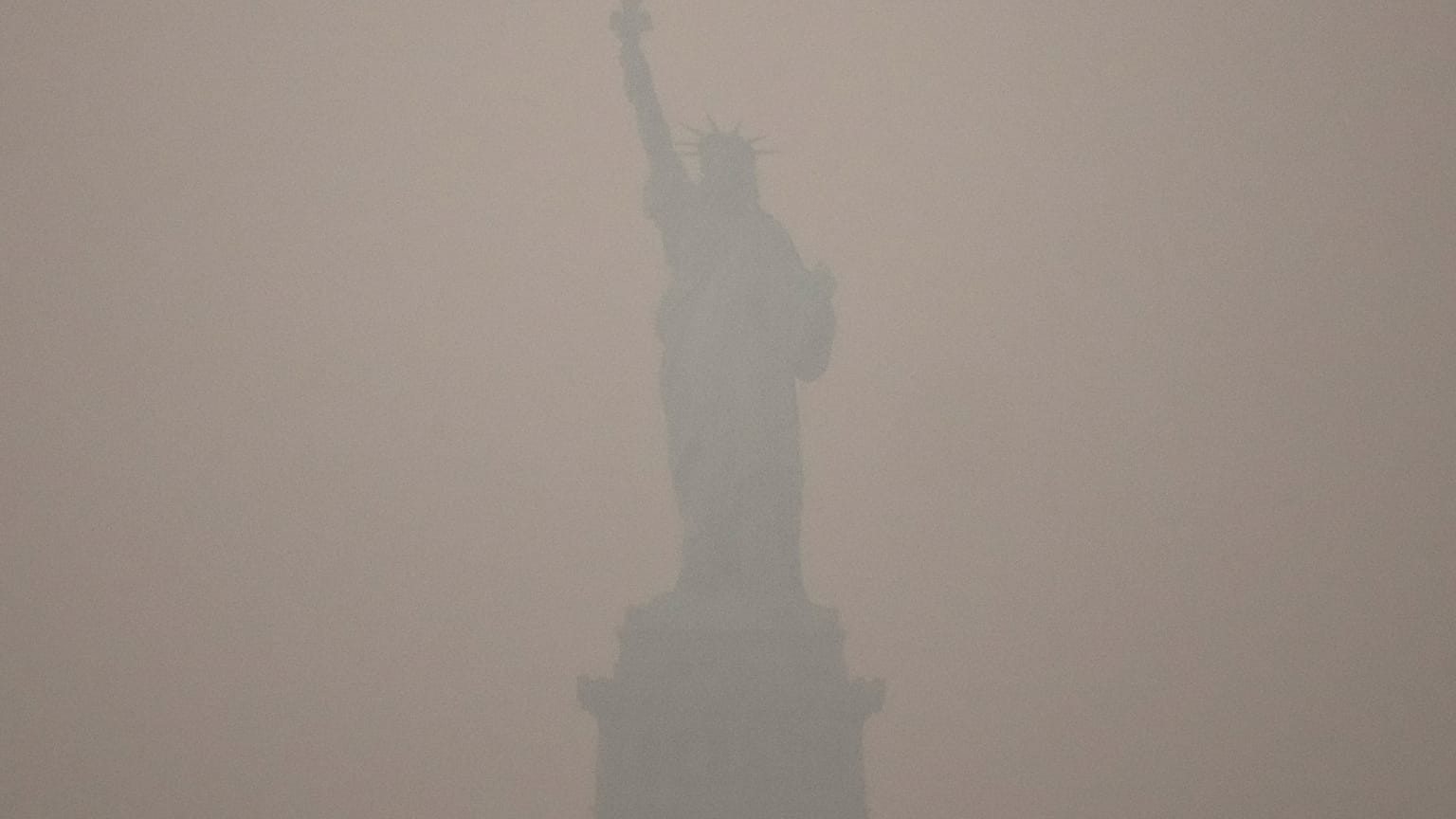 The Statue of Liberty stands during sunset as smoke from wildfires blankets the sky, Thursday, July 16, 2026, in the Brooklyn borough of New York. 