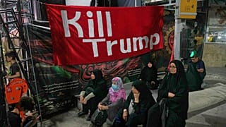 Women sit beneath a banner reading in English, "Kill Trump," during a pro-government rally in Tehran