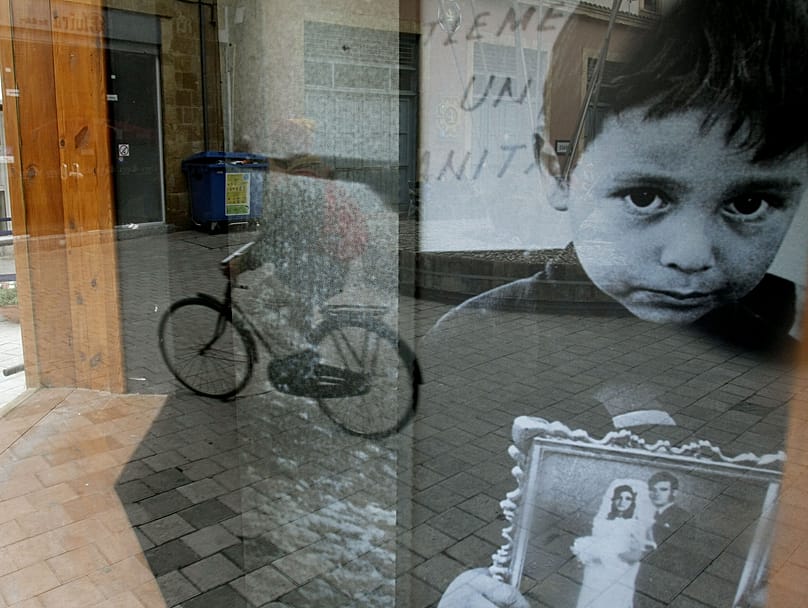 Reflection of a man on a bicycle in front of a glass-covered photo of a boy clutching a picture of his father who disappeared during Turkey's 1974 invasion, Nicosia, 27 Jan 09