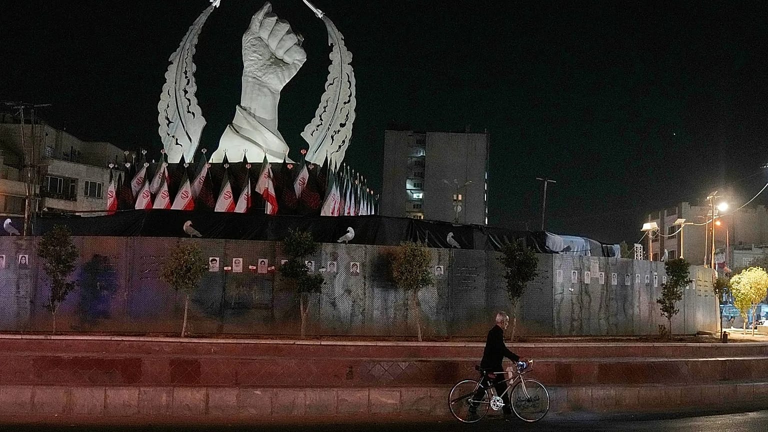 A man carries his bicycle in front of a monument depicting the clenched fist of the late Iranian Supreme Leader Ayatollah Ali Khamenei, who was killed in the U.S. and Israel s
