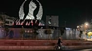 A man carries his bicycle in front of a monument depicting the clenched fist of the late Iranian Supreme Leader Ayatollah Ali Khamenei, who was killed in the U.S. and Israel s