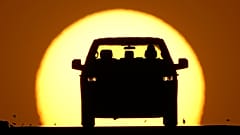 FILE - A motorist is silhouetted by the setting sun