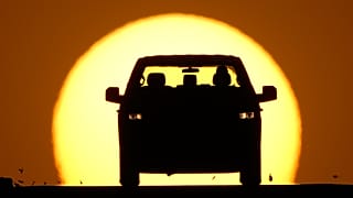 FILE - A motorist is silhouetted by the setting sun