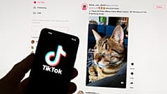 El logo de TikTok en un teléfono, frente a un ordenador con la página de inicio del sitio abierta, al fondo