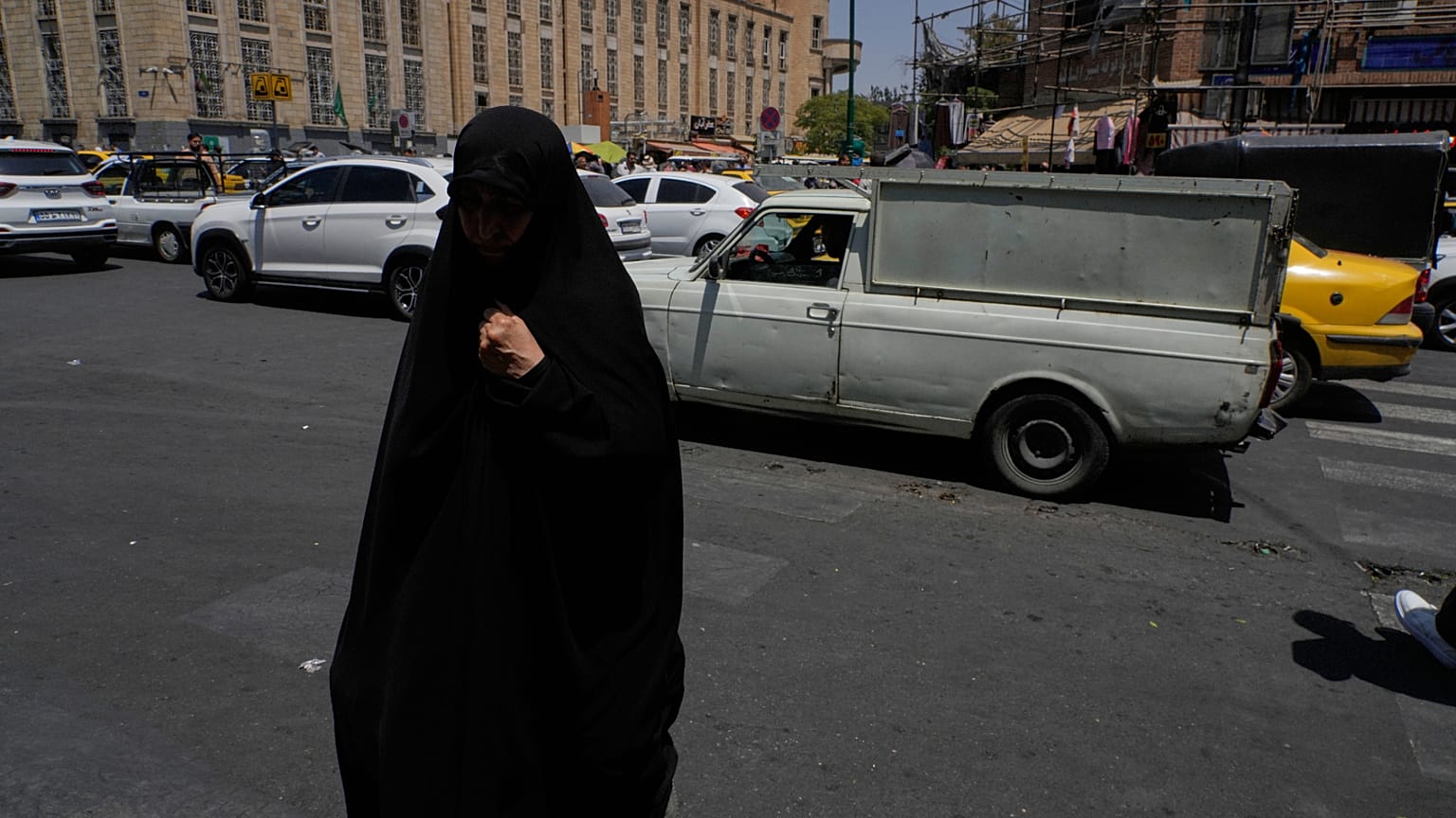 امرأة تمشي بينما تسير المركبات عند تقاطع حول السوق الرئيسي التقليدي في طهران، إيران، الخميس 16 يوليو 2026. (AP Photo/فاهد سليمي)