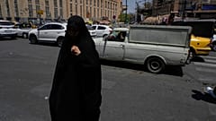 امرأة تمشي بينما تسير المركبات عند تقاطع حول السوق الرئيسي التقليدي في طهران، إيران، الخميس 16 يوليو 2026. (AP Photo/فاهد سليمي)