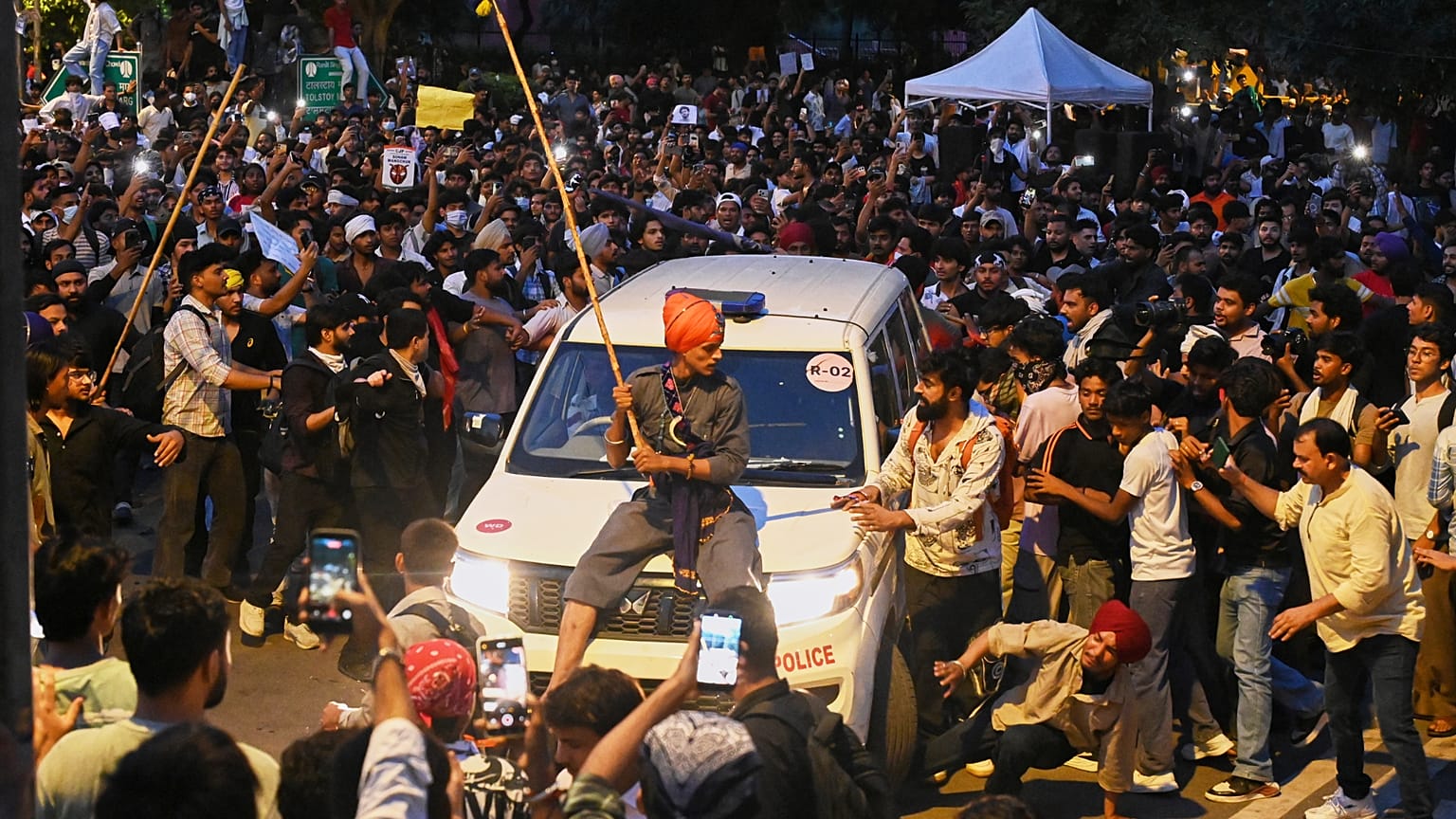 A protestor sits on the hood of a police car during a demonstration demanding educational reforms as part of the Cockroach Janta Party's ongoing protest movement in New Delhi,