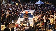 A protestor sits on the hood of a police car during a demonstration demanding educational reforms as part of the Cockroach Janta Party's ongoing protest movement in New Delhi,