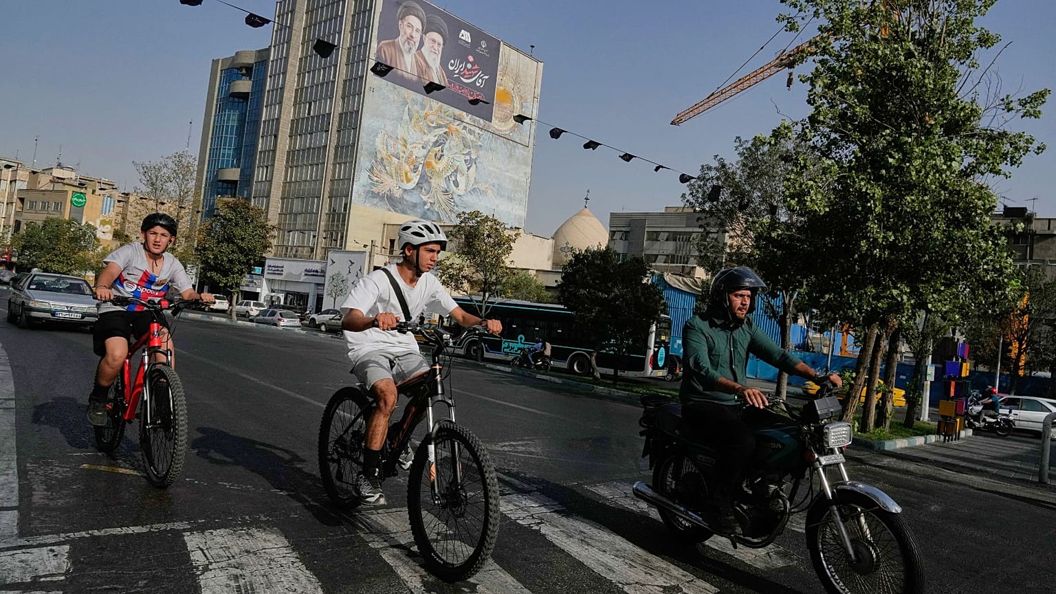 A man rides on his motorbike as boys ride on their bicycles in downtown Tehran, Iran, Wednesday, July 22, 2026. (AP Photo/Vahid Salemi)
