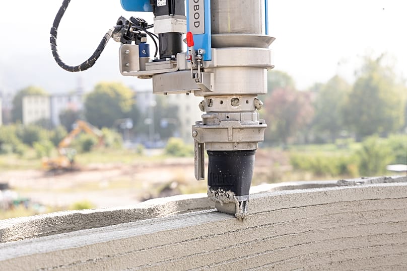 Ein robotergesteuerter Arm trägt den zähflüssigen Spezialbeton Schicht für Schicht auf und formt so die Wände.