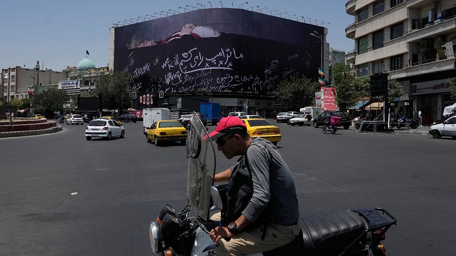 سائق دراجة نارية يمر أمام لوحة في ساحة الثورة الإسلامية بطهران تُظهر ترامب على ما يشبه نعشاً وتحمل عبارة "سنقتل ترامب"