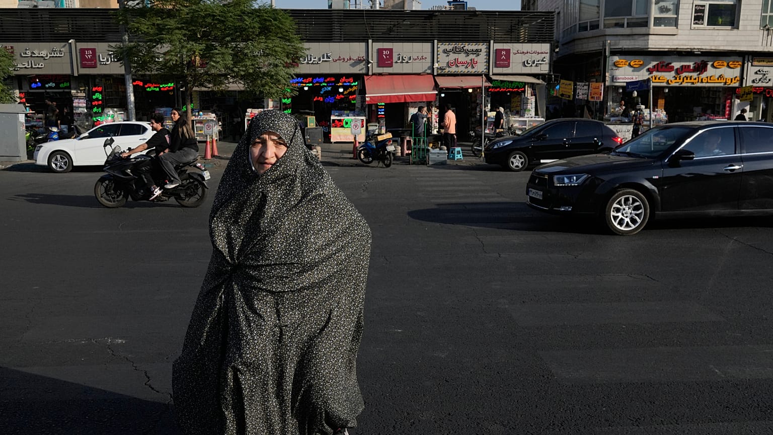 امرأة تمشي بينما تسير المركبات في ساحة الثورة الإسلامية بوسط مدينة طهران، إيران، السبت 18 يوليو 2026. (AP Photo/فاهد سليمي)