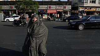 امرأة تمشي بينما تسير المركبات في ساحة الثورة الإسلامية بوسط مدينة طهران، إيران، السبت 18 يوليو 2026. (AP Photo/فاهد سليمي)