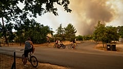 Varias personas observan las enormes columnas de humo provocadas por los incendios forestales en Le Porge, en el oeste de Francia, el jueves 23 de julio de 2026.