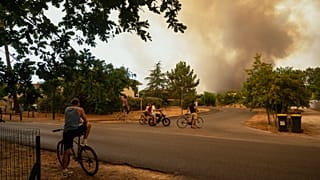 People watch massive plumes of smoke caused by wildfires in Le Porge, western France, Thursday, July 23, 2026.