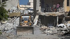 شباب فلسطينيون يراقبون جرافة تزيل الأنقاض من شارع تضرر جراء الهجوم الجوي والبري الإسرائيلي في رفح، جنوب قطاع غزة، يوم الثلاثاء، 21 يناير 2025.