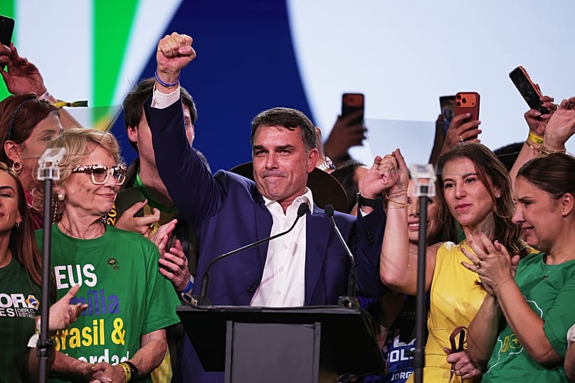 Flávio Bolsonaro, ao centro, e a sua esposa Fernanda levantam os braços em uníssono durante a convenção do Partido Liberal, na qual Bolsonaro foi confirma a sua candidatura.