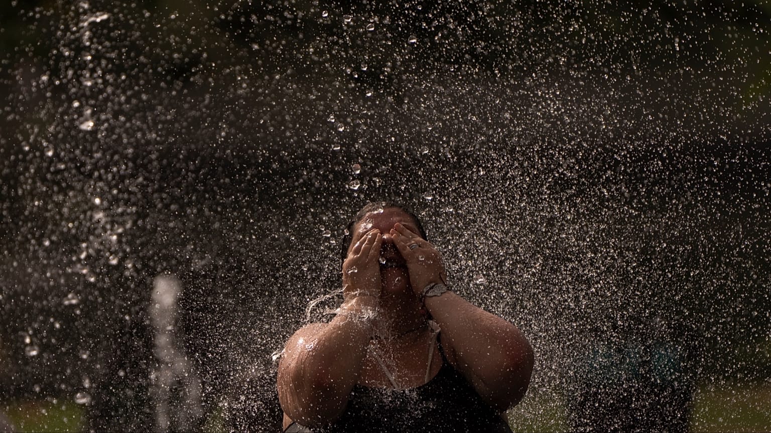 Una donna si rinfresca in una fontana in un parco lungo il fiume a Madrid, in Spagna, mercoledì 15 giugno 2022.
